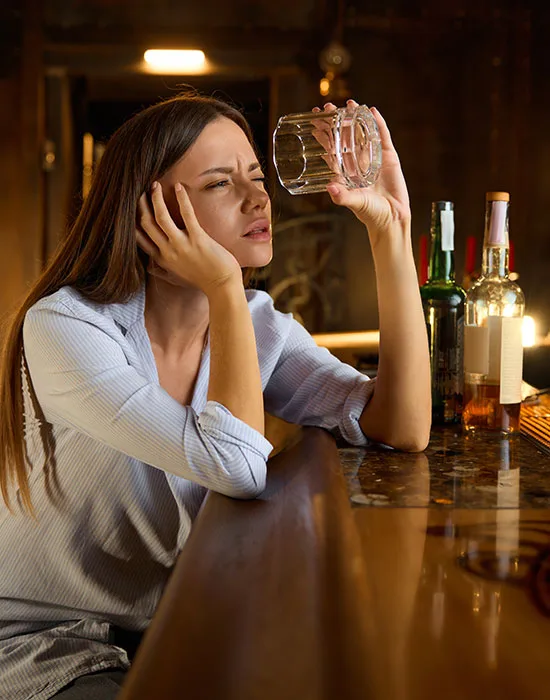 A Woman At A Bar Clutches A Glass Of Alcohol, Representing Her Challenges With Addiction.